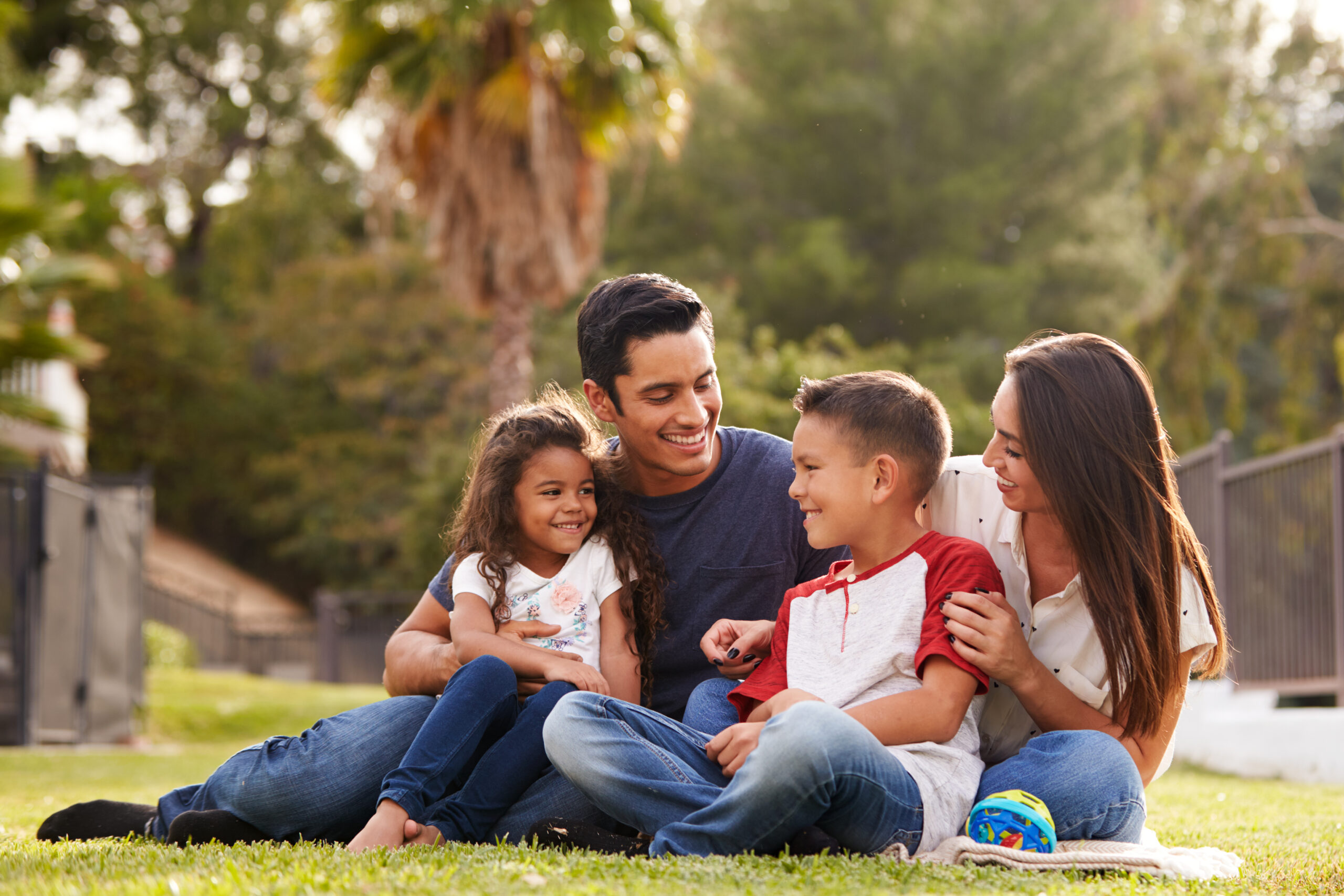 Happy,Young,Hispanic,Family,Sitting,Together,On,The,Grass,In